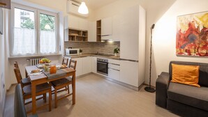 A modern kitchen with white cabinetry, a dining table with chairs, and a sofa in the living area. - STRAMBIO, 8 – Smart Stay in Milan (Milano)