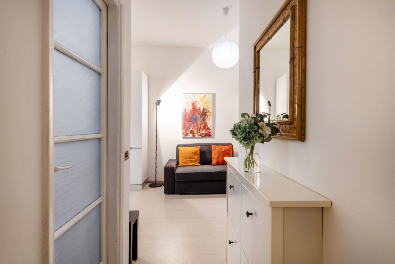 A hallway with a sofa, a mirror, and a painting on the wall.