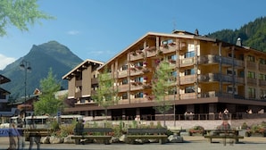 Un hotel de varios pisos con balcones, mobiliario exterior y montañas al fondo.