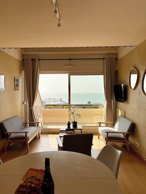 A hotel room with a balcony, a table with chairs, a TV, and a bottle on the table. - Saint-Malo duplex, ocean view, beach, parking, charging station, waterfront (Saint-Malo)