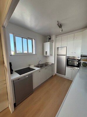 A modern kitchen with white cabinets, a stainless steel refrigerator, a dishwasher, and a windowed sink. - Saint-Malo duplex, ocean view, beach, parking, charging station, waterfront (Saint-Malo)