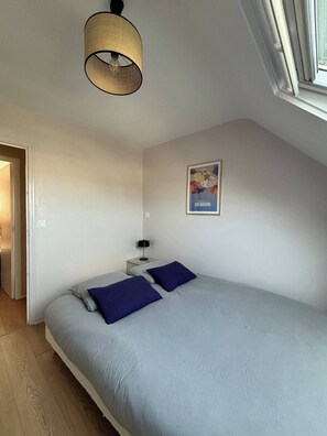 A bedroom with a bed, a nightstand, a lamp, and a poster on the wall. - Saint-Malo duplex, ocean view, beach, parking, charging station, waterfront (Saint-Malo)