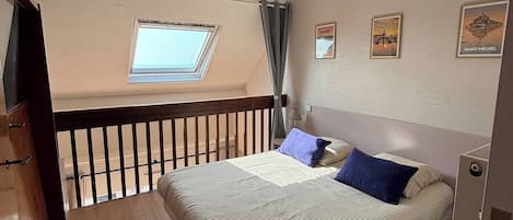 Une chambre avec un grand lit, une lucarne et un balcon.