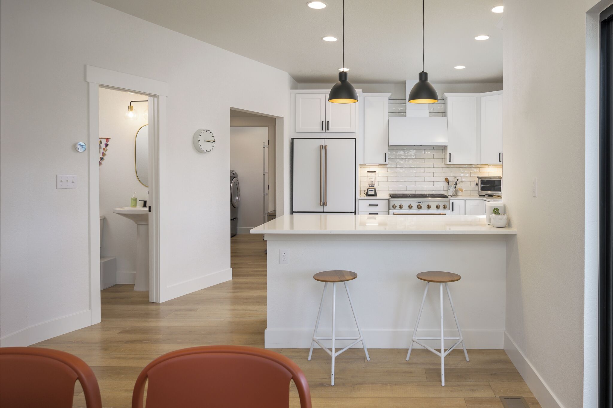 Une cuisine moderne avec des meubles blancs, un îlot central doté de tabourets et un éclairage suspendu.