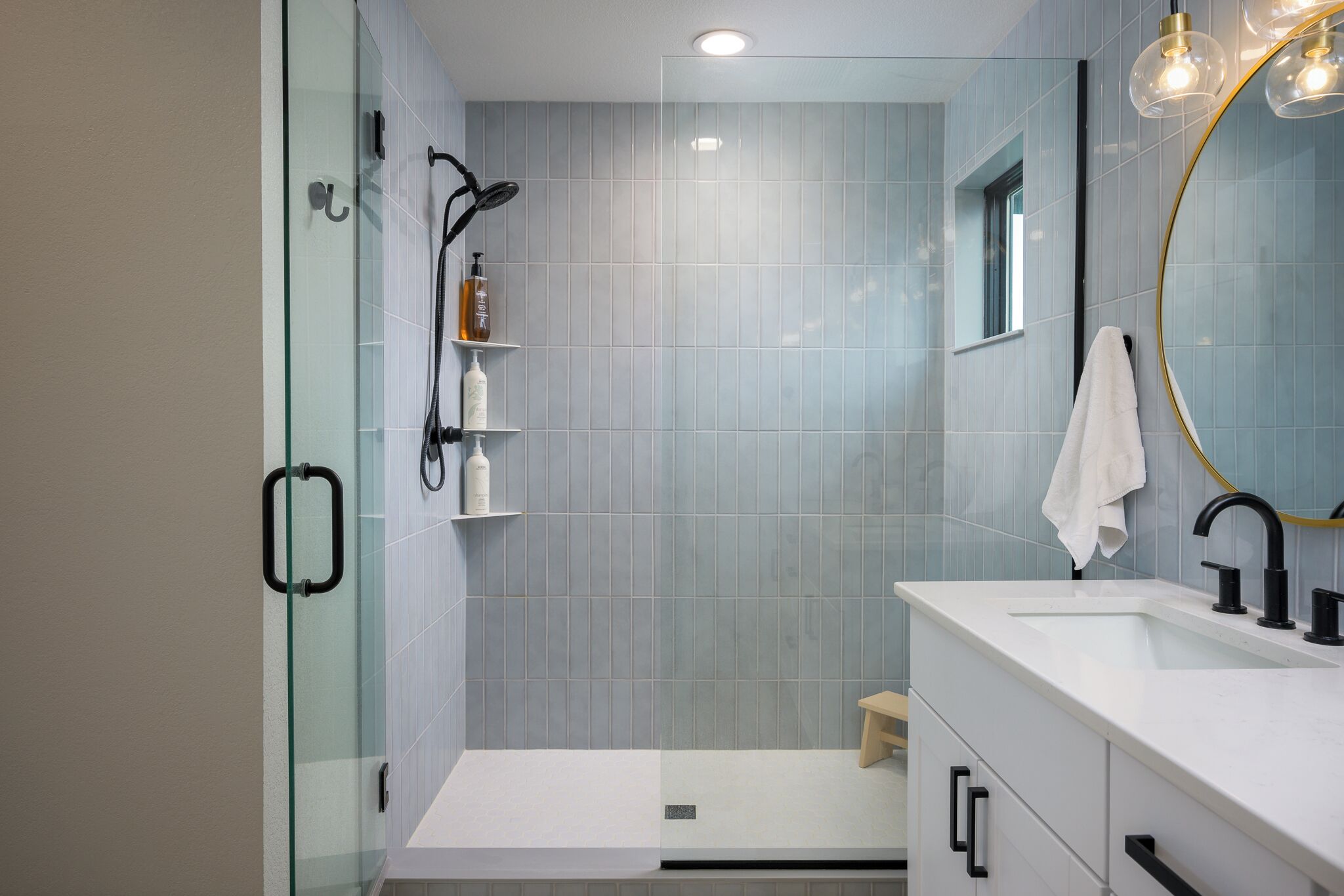 Un baño moderno con cabina de ducha de vidrio, tocador blanco con un espejo grande y ducha a pie.