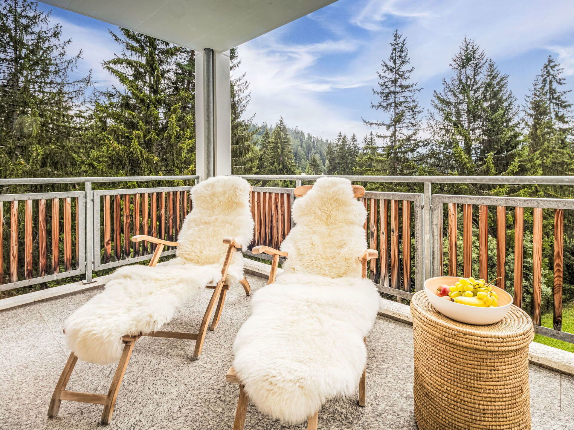 A balcony with two lounge chairs and a wicker table with fruit.