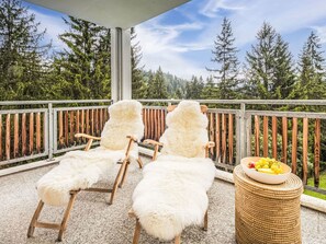 Ein Balkon mit zwei Liegestühlen und einem Korbstuhl-Tisch mit Früchten.