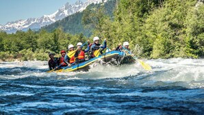 Un grupo de personas hacen rafting en un río con montañas al fondo.
