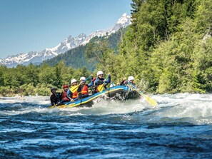 Eine Gruppe von Menschen treibt auf einem Fluss, mit einer Berglandschaft im Hintergrund.