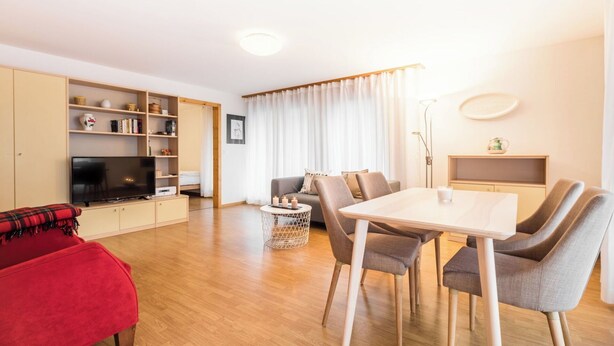 Una sala de estar moderna con un sofá rojo, una mesa de comedor con sillas, un televisor y una estantería.