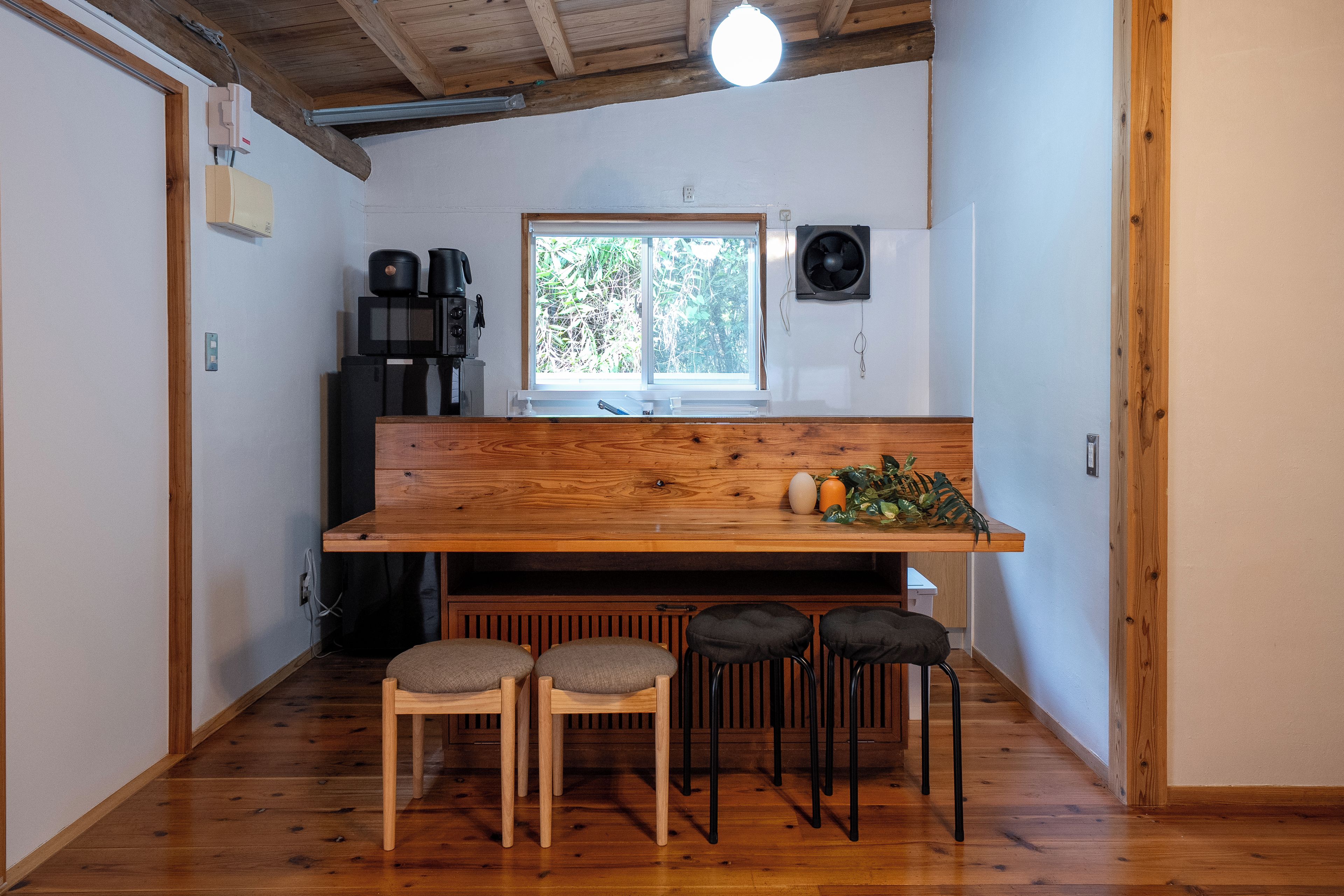 Cocina compacta con encimera de madera, ventana y lavamanos. Hay tres taburetes y una cafetera.