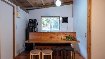Cocina compacta con encimera de madera, ventana y lavamanos. Hay tres taburetes y una cafetera.