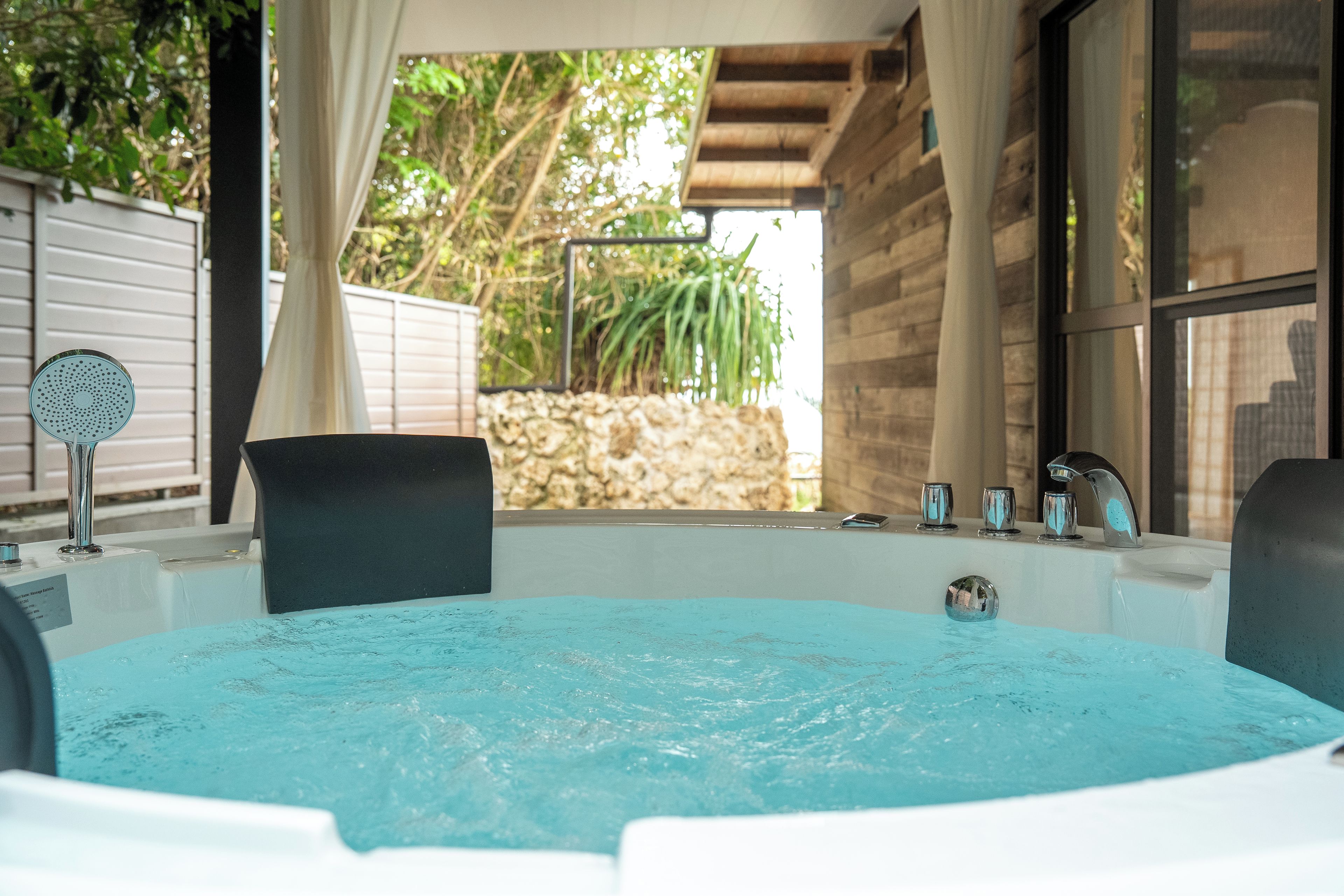 Un jacuzzi con pared de piedra y follaje de fondo.