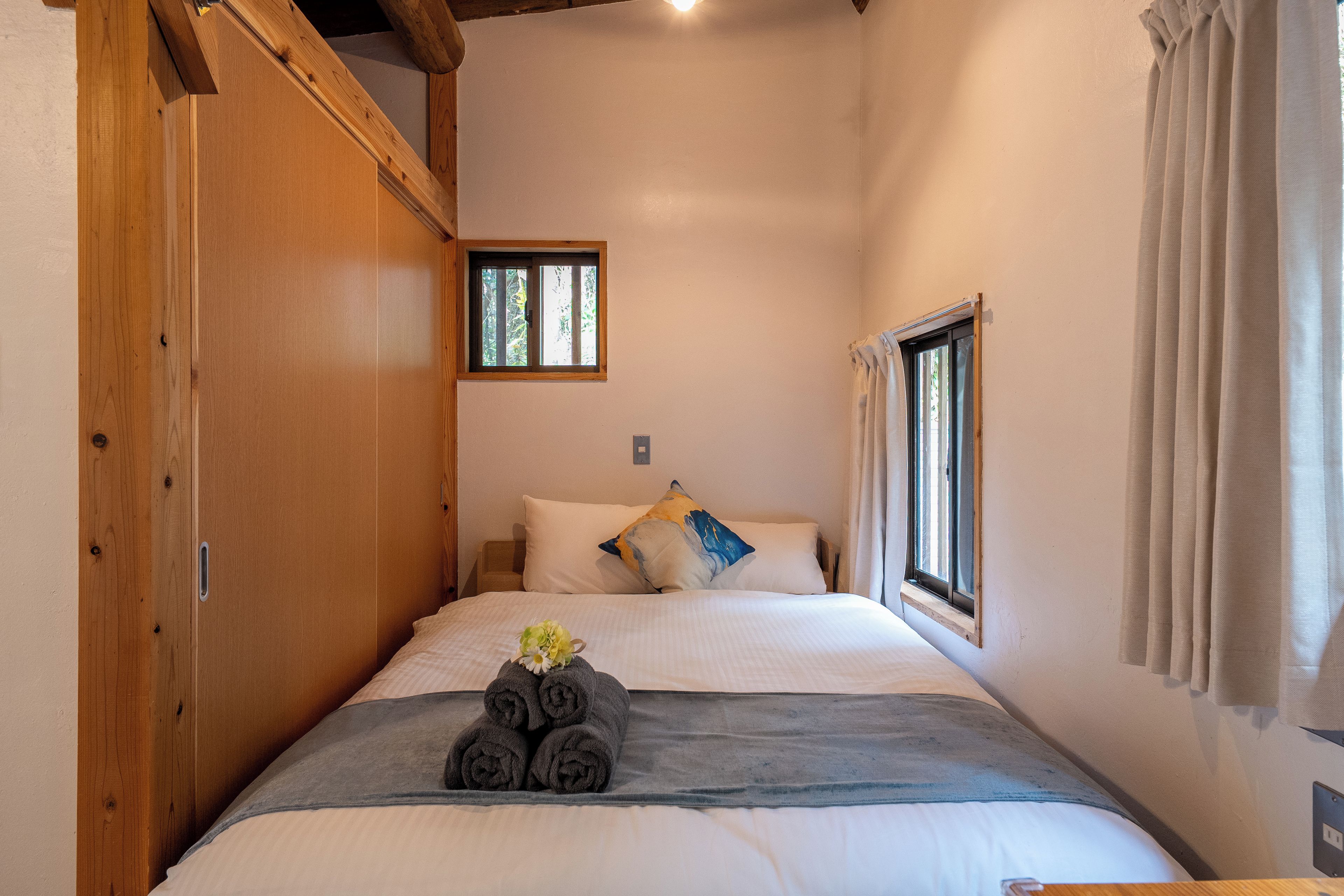 Ein Schlafzimmer mit einem Holzschrank, einem Bett mit weißer Bettw äsche, einem Fenster mit Blick und einem kleinen Nachttisch.