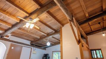 A room with wooden beams, a ceiling fan, a window, and a kitchenette with appliances.