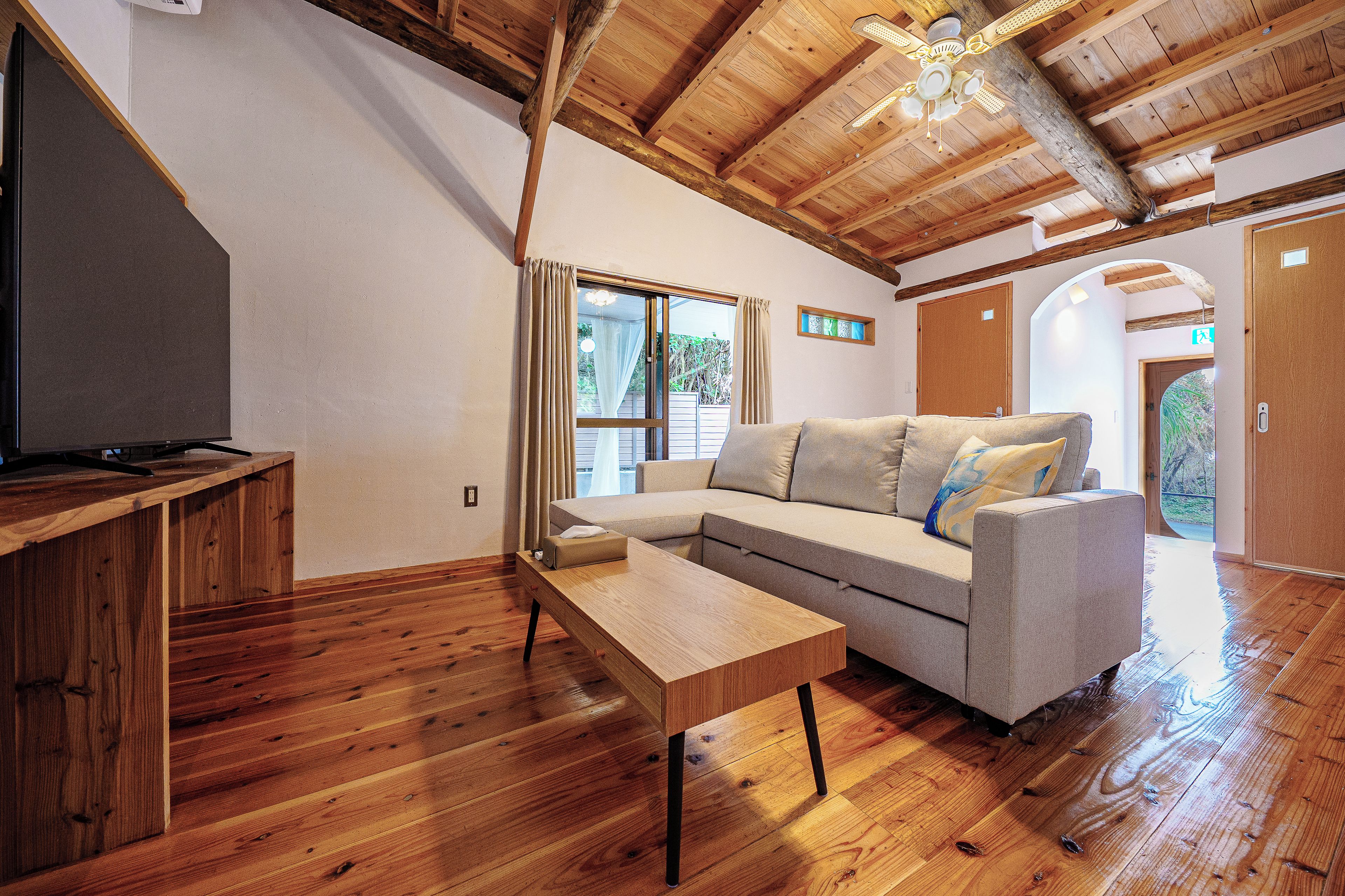 Una habitación con piso de madera, un sofá, una mesita y un ventilador de techo.