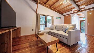 Una habitación con piso de madera, un sofá, una mesita y un ventilador de techo.