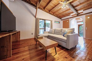 Una habitación con piso de madera, un sofá, una mesita y un ventilador de techo.