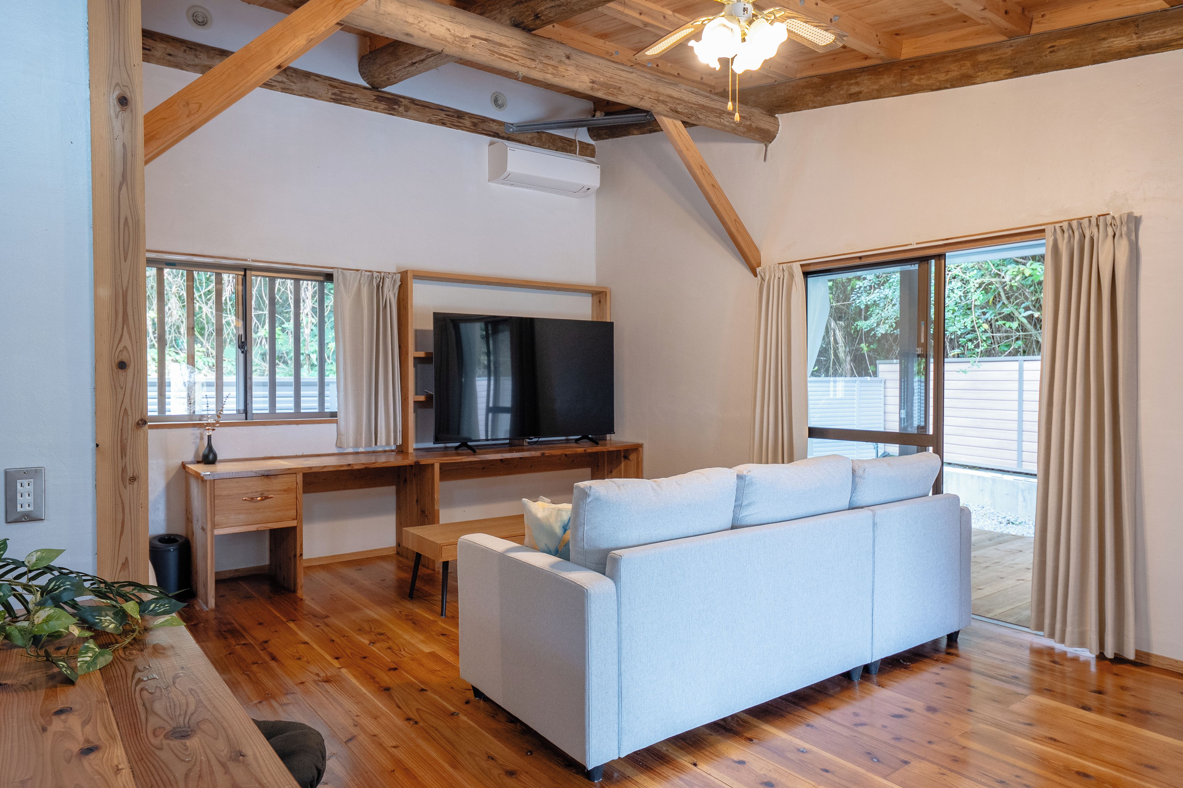 Une pièce spacieuse avec un plafond en bois, un téléviseur posé sur un meuble en bois, un canapé et un bureau avec une chaise.