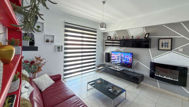 A modern living room with a red sofa, a coffee table, a flat-screen TV, and a fireplace. - Family Resort Apt with Pool Sleeps 6 (Paralimni)