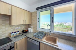 Cocina moderna con lavavajillas, un lavabo y una ventana con vistas a edificios y vegetación.