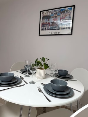 A dining table set with plates, bowls, cutlery, and glasses, with a framed picture of Oxford on the wall. - Modern Annexe, 10 Minutes from Oxford City Centre (Oxford)
