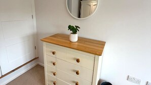Een witte dressoir met houten bovenblad en lades, een ronde spiegel aan de muur, en een prullenbak.