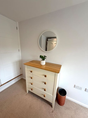 A white dresser with wooden top and drawers, a round mirror on the wall, and a trash bin. - Modern Annexe, 10 Minutes from Oxford City Centre (Oxford)