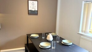 A dining area with a table set for four, a framed picture on the wall, and a window to the right. - Market Place Retreat (Oxfordshire)