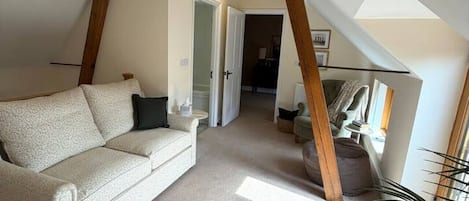 Une pièce de style « loft », avec un plafond haut, un canapé blanc, une structure en poutres apparentes et une vue sur une autre pièce.