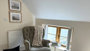 A cozy room with a large window, a radiator, a chair, a bean bag, and two framed pictures on the wall. - Market Place Retreat (Oxfordshire)