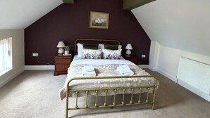 A bedroom with a sloped ceiling, a bed with a metal frame, a bedside table with a lamp, and a framed picture on the wall. - Market Place Retreat (Oxfordshire)