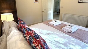 Hotellihuone, jossa on sänky, yöpöytälamppu, ovi kylpyhuoneeseen ja seinällä oleva kehystetty kuva.