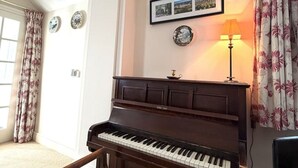 Huoneessa on piano, tuoli, lamppu ja verhot.