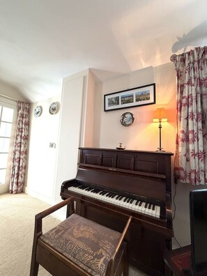 A piano in a room with a chair, a lamp, and curtains. - Charming Countryside Escape & Private Tennis Court (Denchworth)