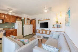 Ein modernes Wohnzimmer mit einer Couch, einem Fernseher und einer Küchenzeile mit Holzausbau und einem Kühlschrank.