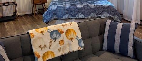 A bedroom with a bed, a sofa, a lamp, and a window with curtains.
