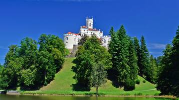 A castle with a tower, surrounded by trees and a body of water.
