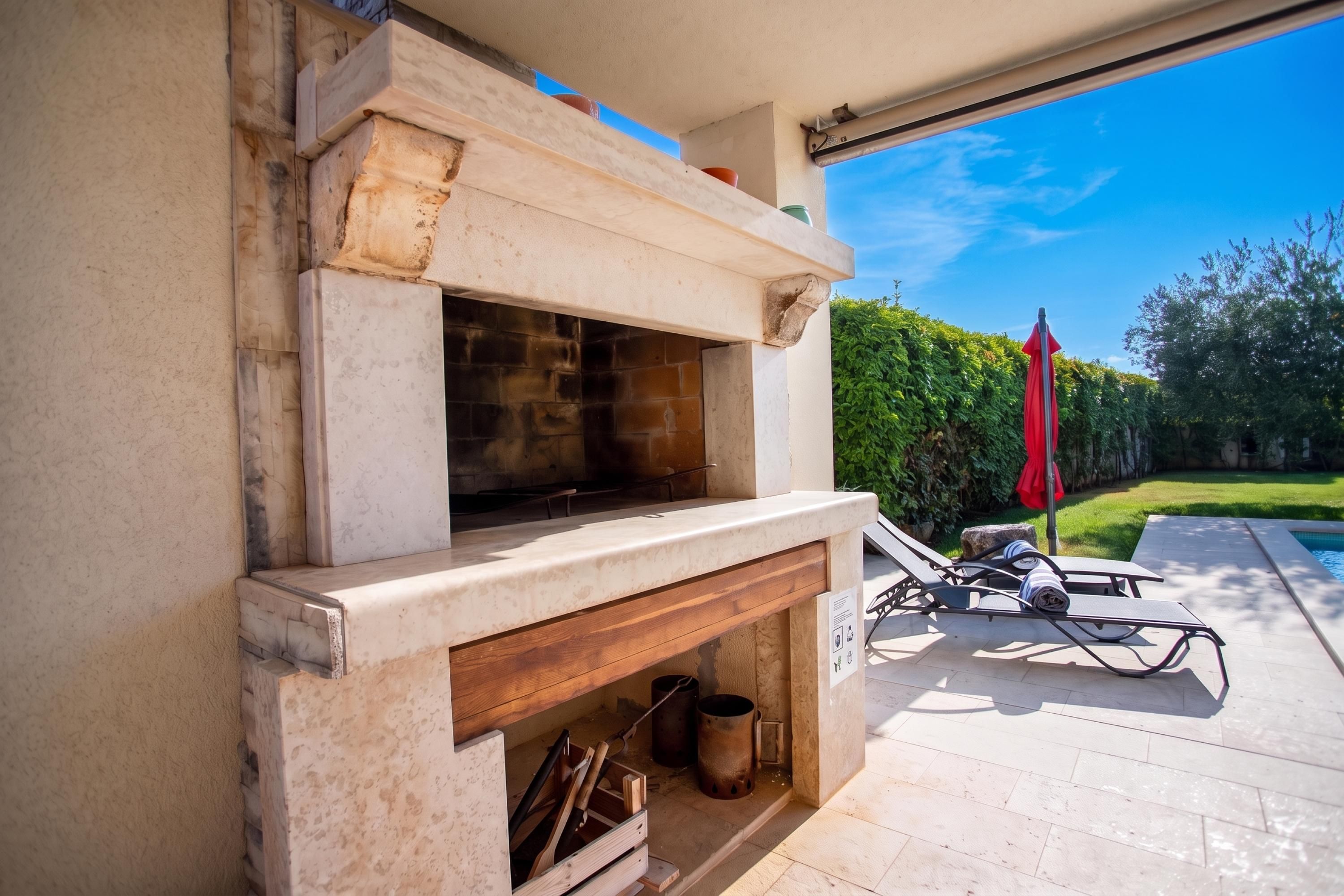 An outdoor fireplace with a stone surround, a wooden bench, and a red umbrella.