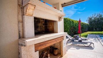 An outdoor fireplace with a stone surround, a wooden bench, and a red umbrella.