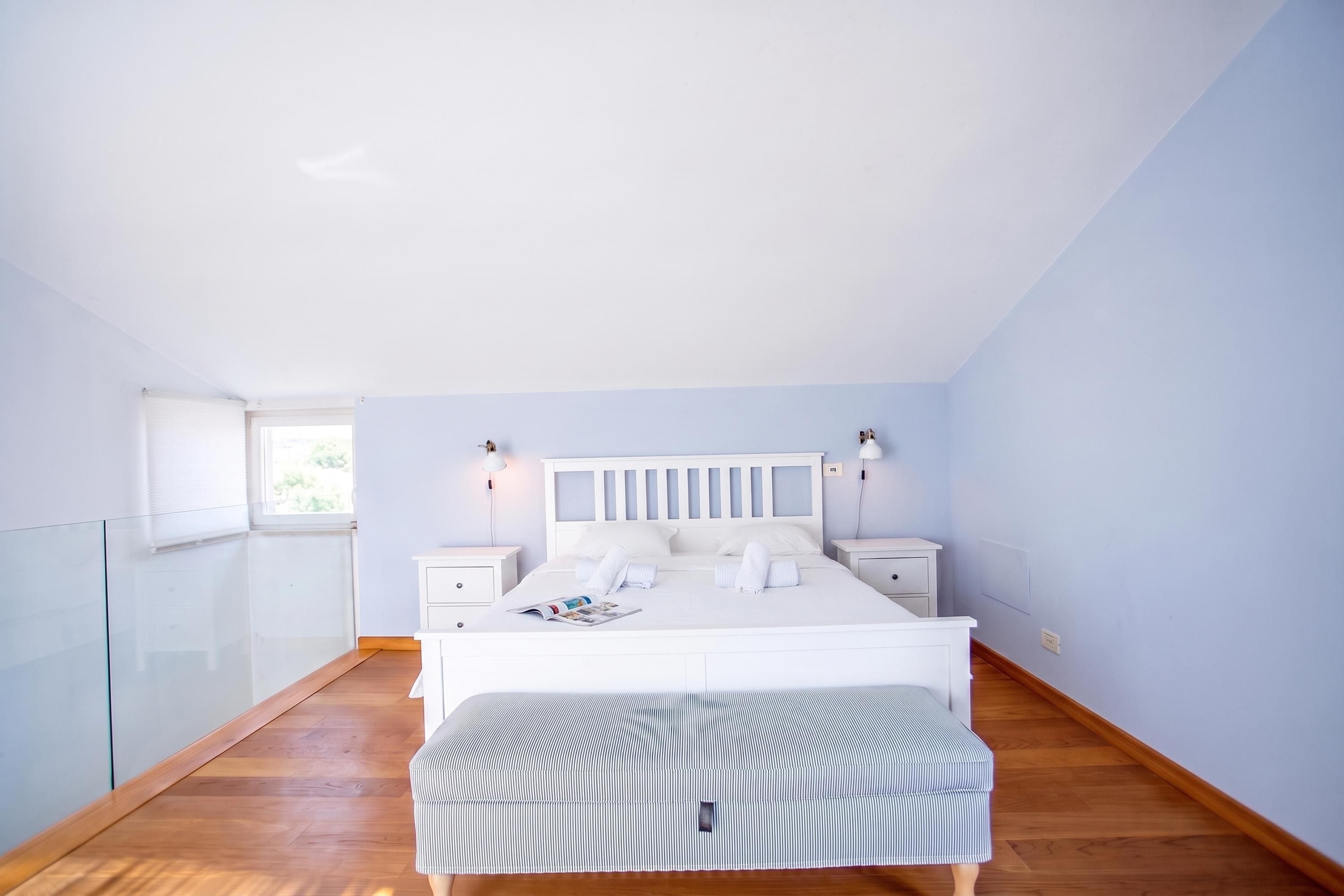 Un dormitorio con una cama, mesitas de noche, un banco y una ventana.