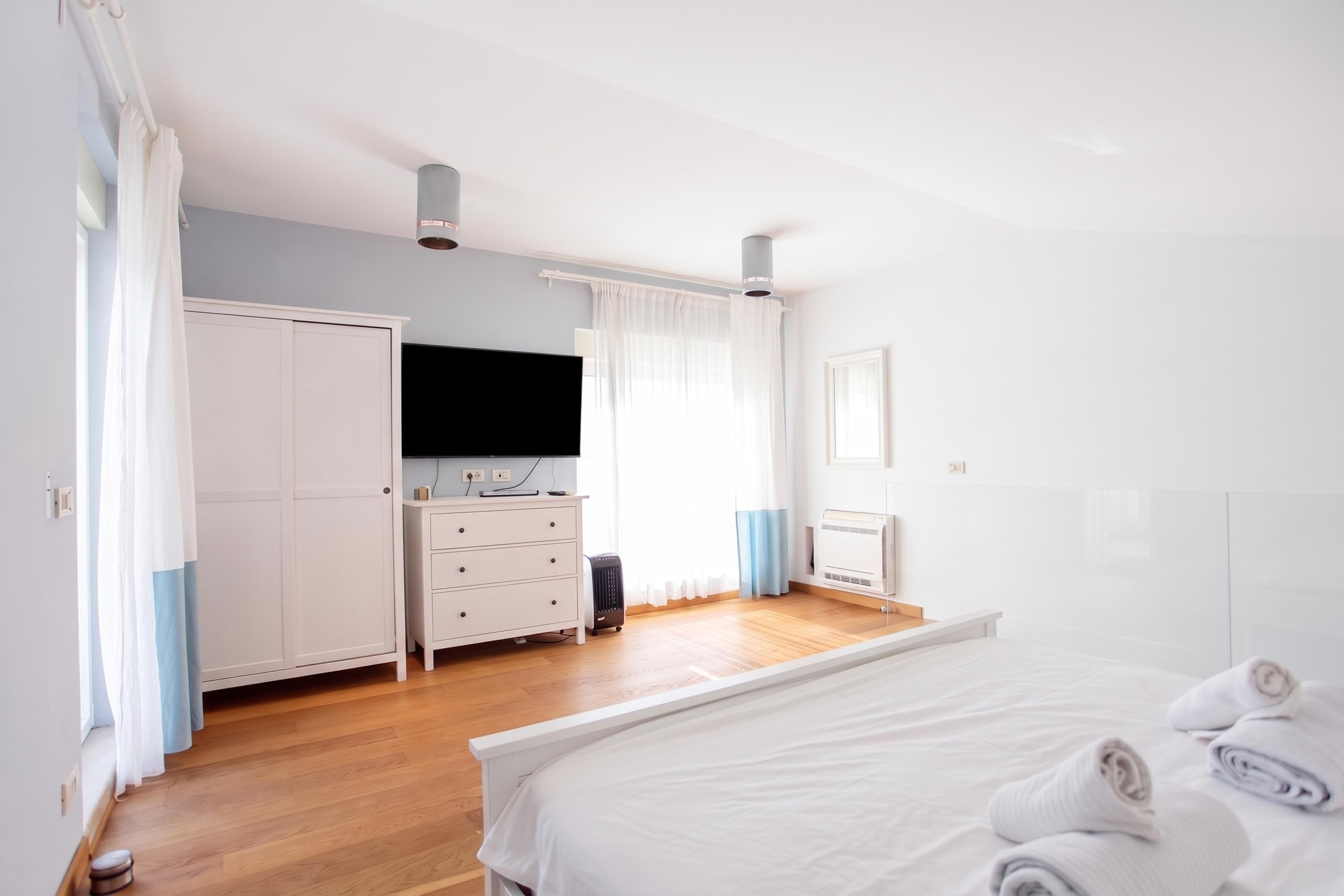 A bedroom with a bed, a dresser, a television, and a heater.