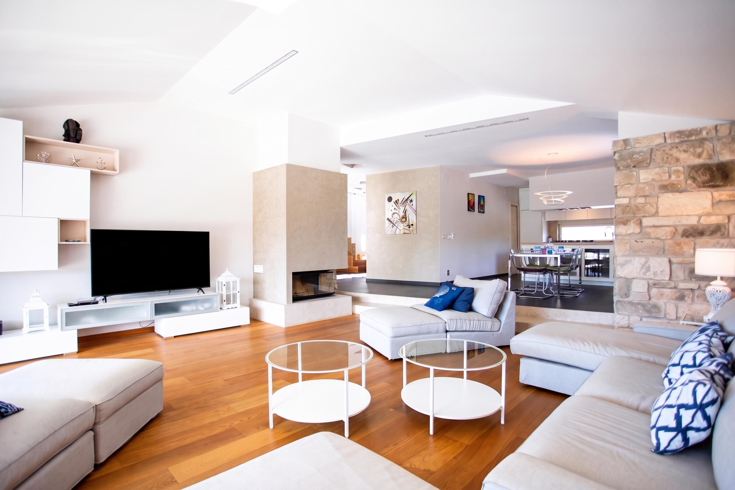 Una sala de estar moderna con televisor de pantalla plana, chimenea, comedor y cocina con detalles de piedra.
