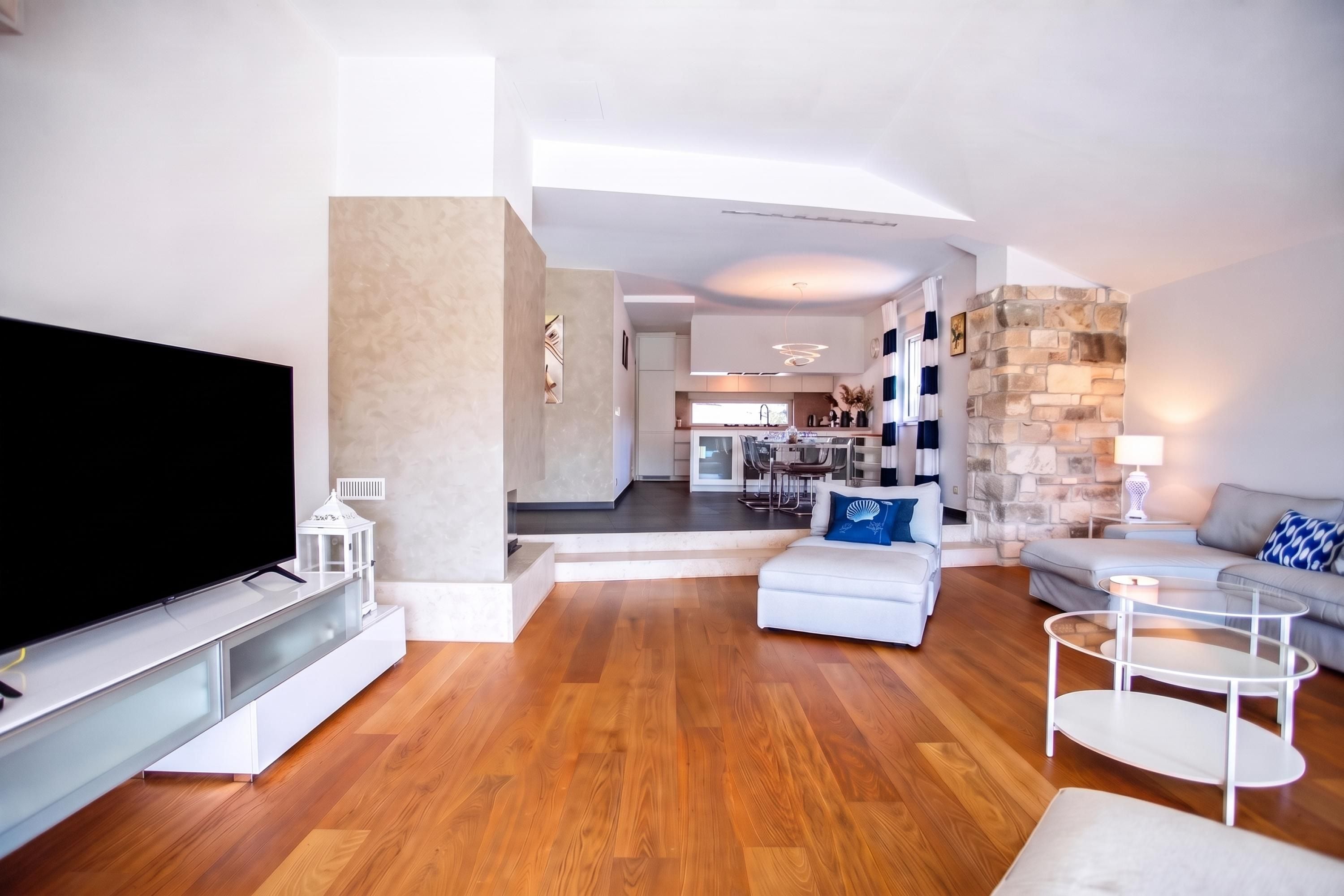 A modern living room with a flat-screen TV, a sofa, a coffee table, and a dining area in the background.