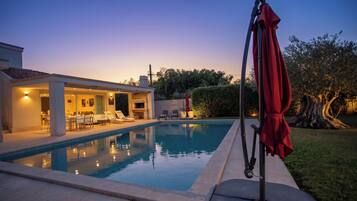 A swimming pool with lounge chairs and a covered area, surrounded by a well-maintained lawn and trees.