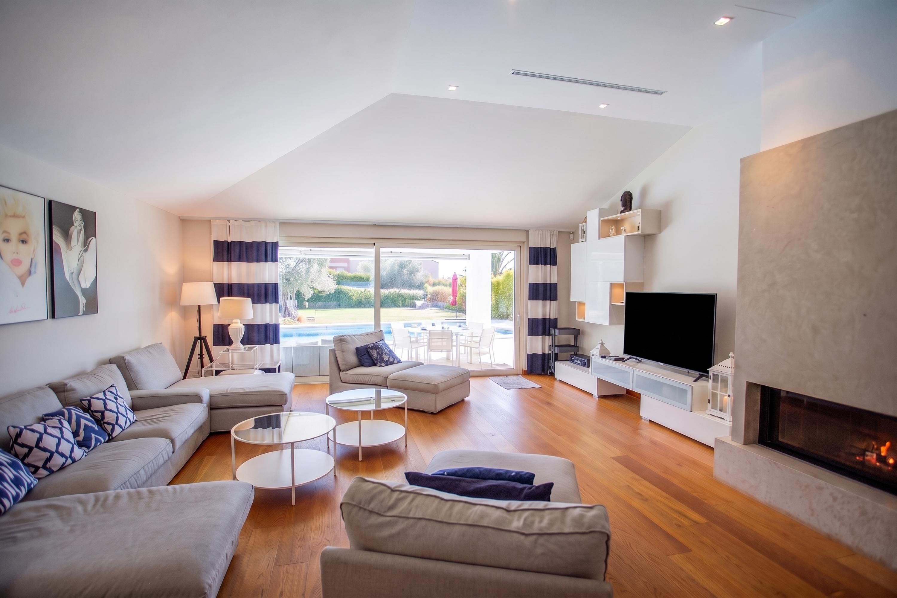 A modern living room with a sofa, coffee table, and TV. There is a fireplace and a view of a pool outside.
