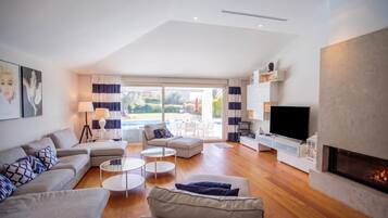 A modern living room with a sofa, coffee table, and TV. There is a fireplace and a view of a pool outside.