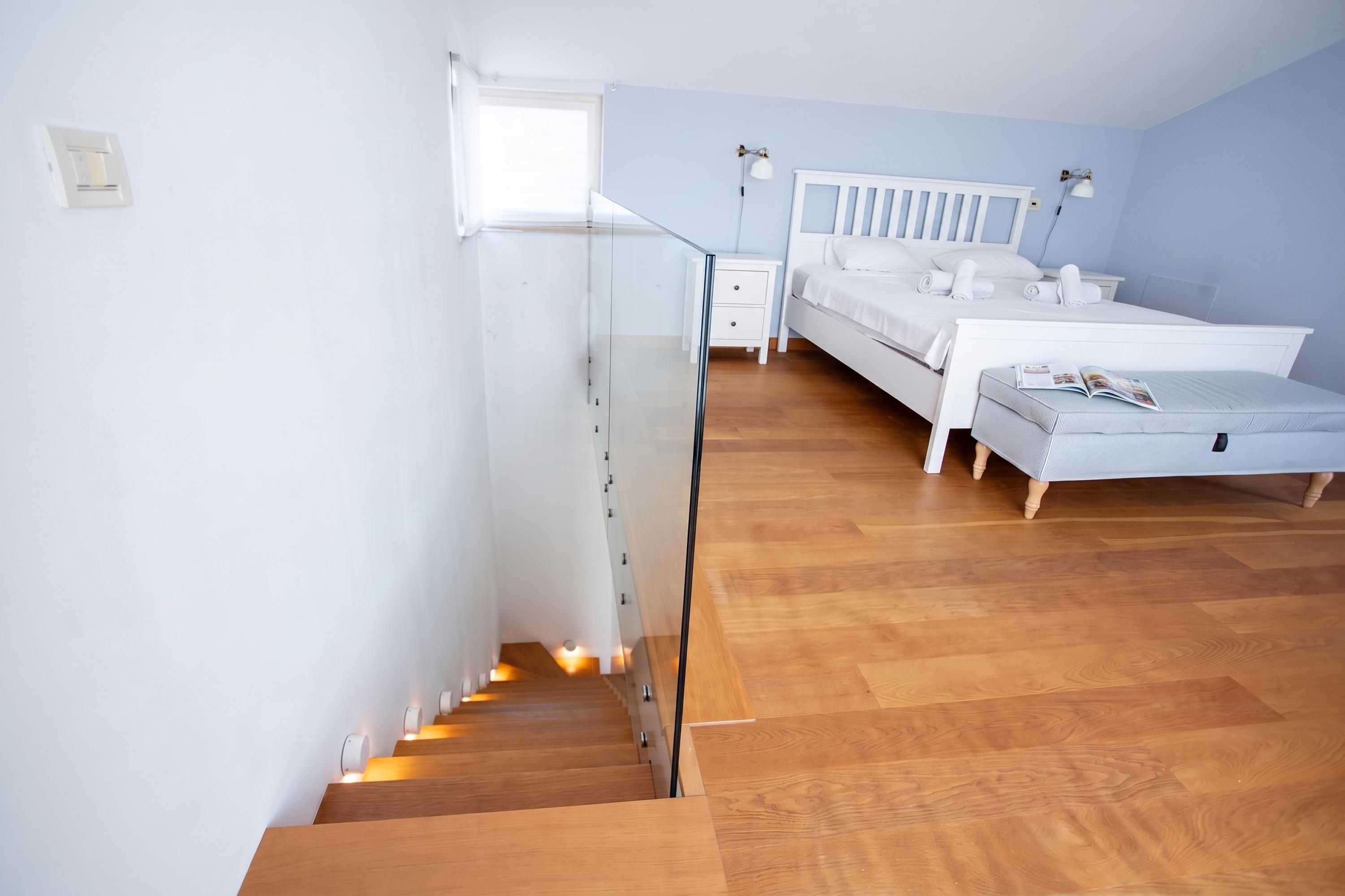A bedroom with a wooden staircase, a bed, a bedside table, and a window.