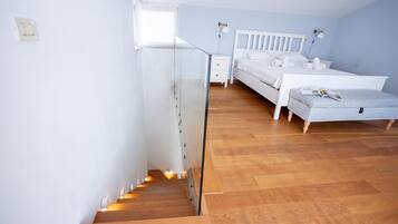 A bedroom with a wooden staircase, a bed, a bedside table, and a window.
