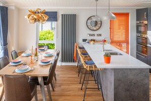 Een moderne keuken met een centraal eiland, een eethoek met stoelen en uitzicht op groen.